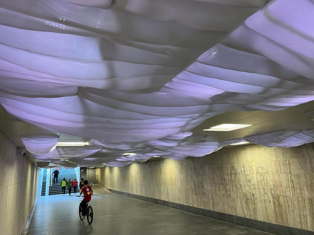 A pedestrian underpass transformed by a soft, cloud-like LED ceiling installation that creates a calm and immersive atmosphere.